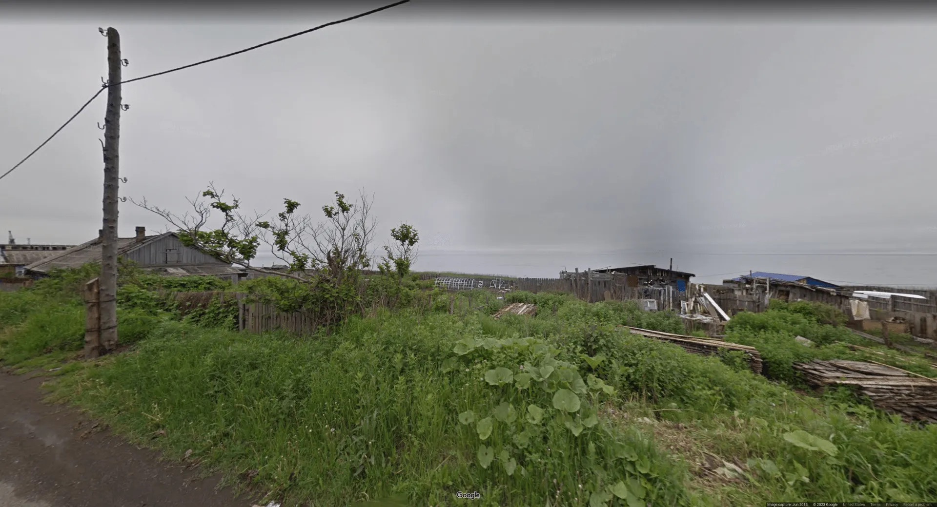 Image of dilapidated sheds and fences next to an ocean, with overcast skies