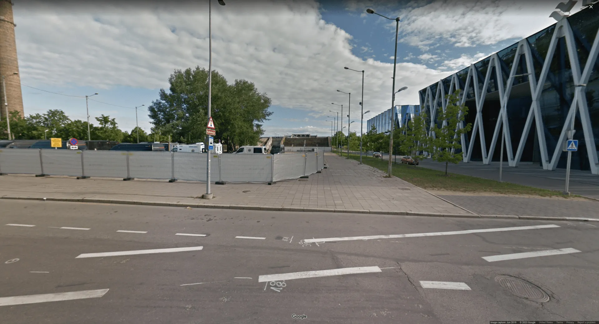 Picture of an empty sidewalk in a European business district. There is a lamppost in the center-left of the screen with directional signs on it