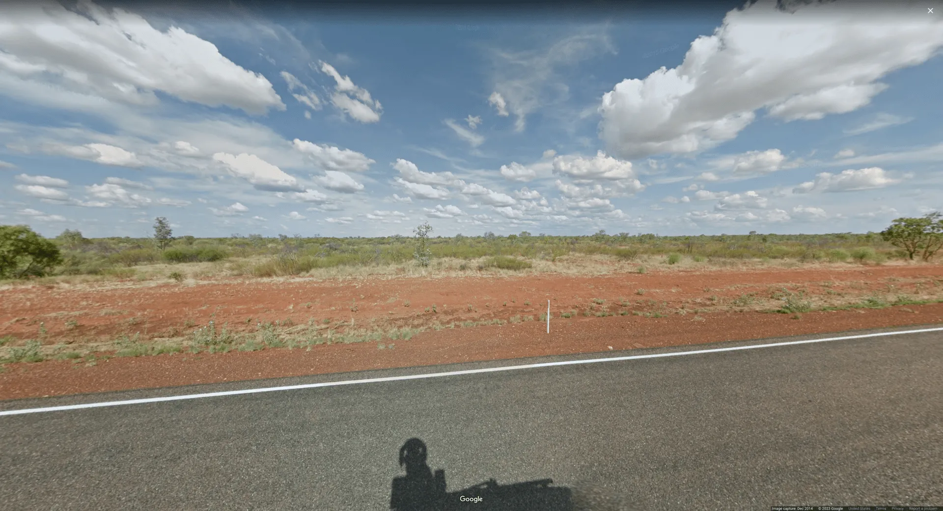 Picture of the side of a rural highway, with patchy grass and reddish soil