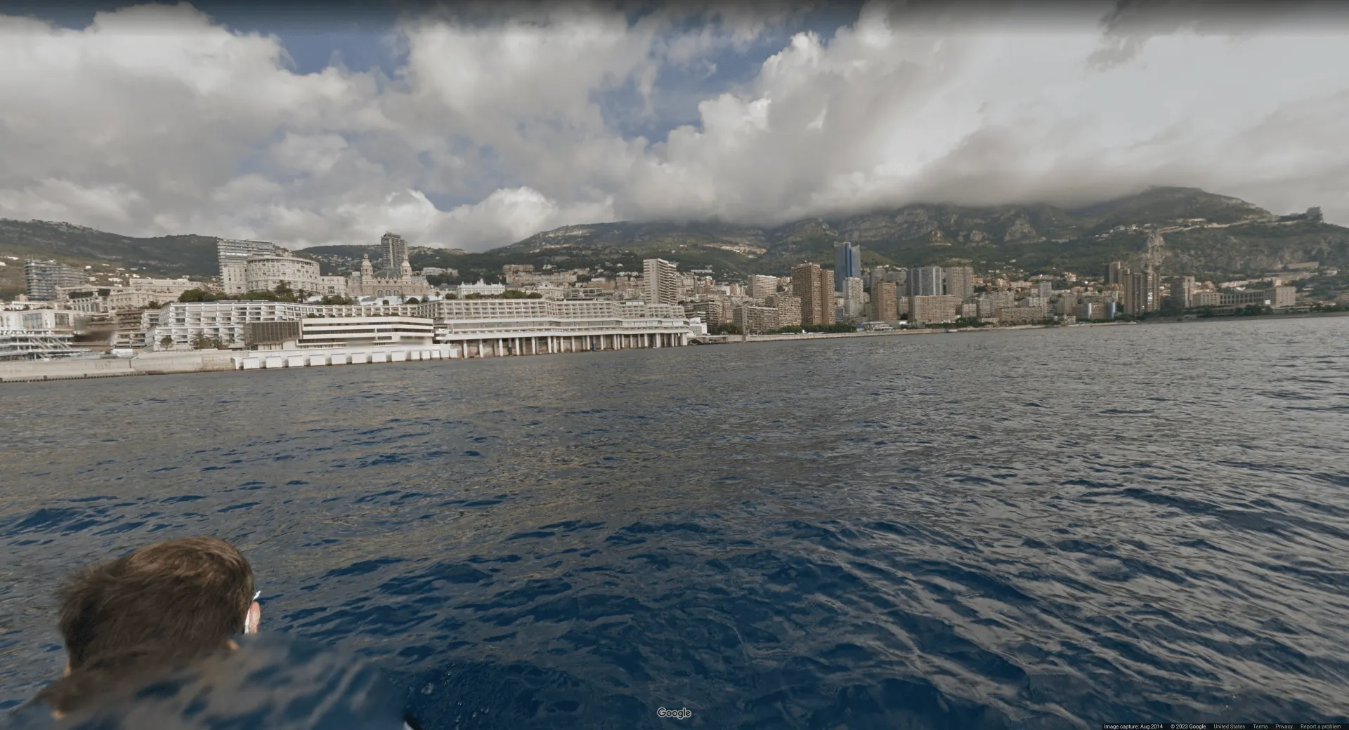 Picture taken in the water off the shore of a large city's downtown area. The buildings are mostly white and there are hills in the background